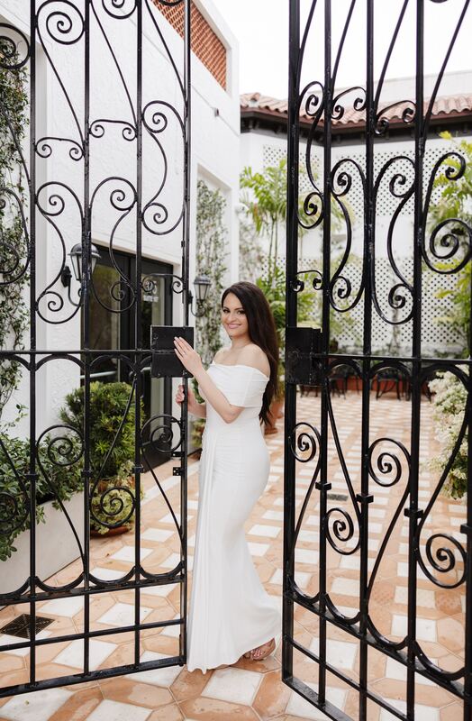 Iviani standing at an ornate wrought-iron gate in a white gown