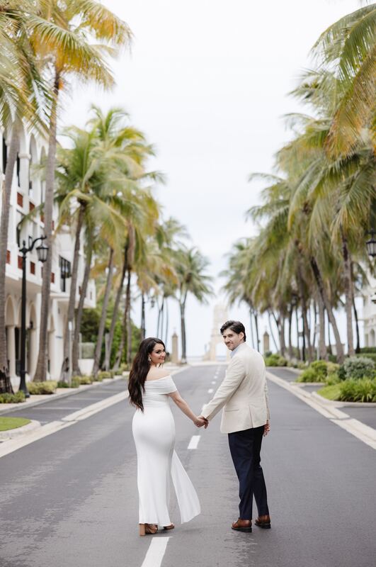 Iviani and Joey holding hands in the middle of a palm-lined avenue