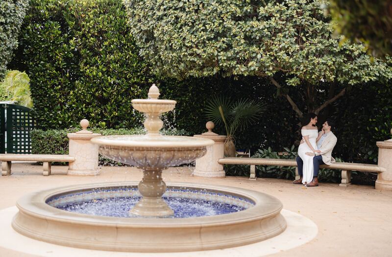 Iviani and Joey seated by a tiled fountain in a garden courtyard