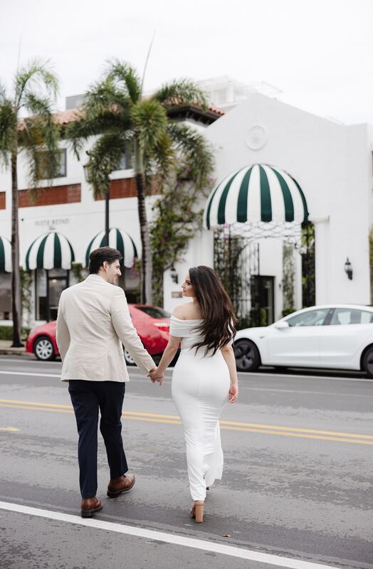 Iviani and Joey crossing the street hand in hand beneath striped awnings
